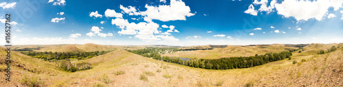 Summer panorama of the hilly terrain of the steppe lake, trees and village.