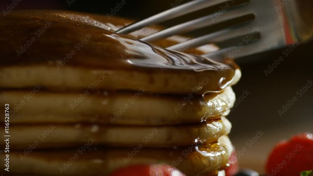 Silver fork cutting into a stack of maple drizzled pancakes, in slow motion 