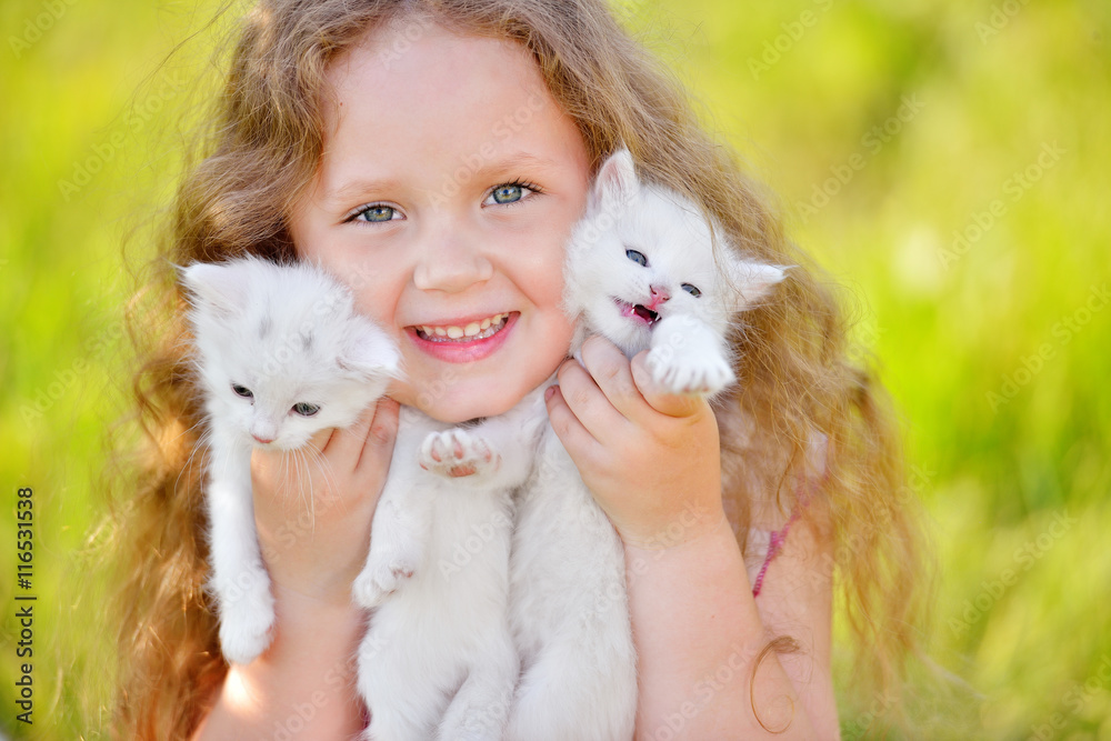 Adorable little girl playing with small kittens at summer day