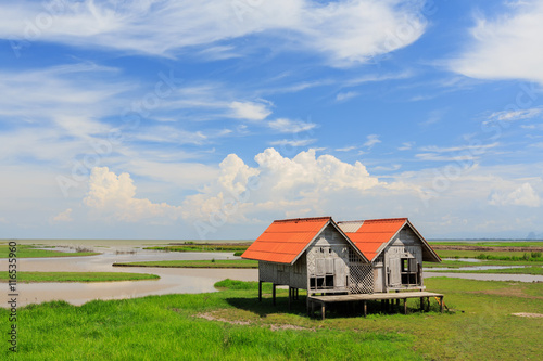 Blue skies, white clouds, green grass, & open range land dominate in Thailand with abandoned hut