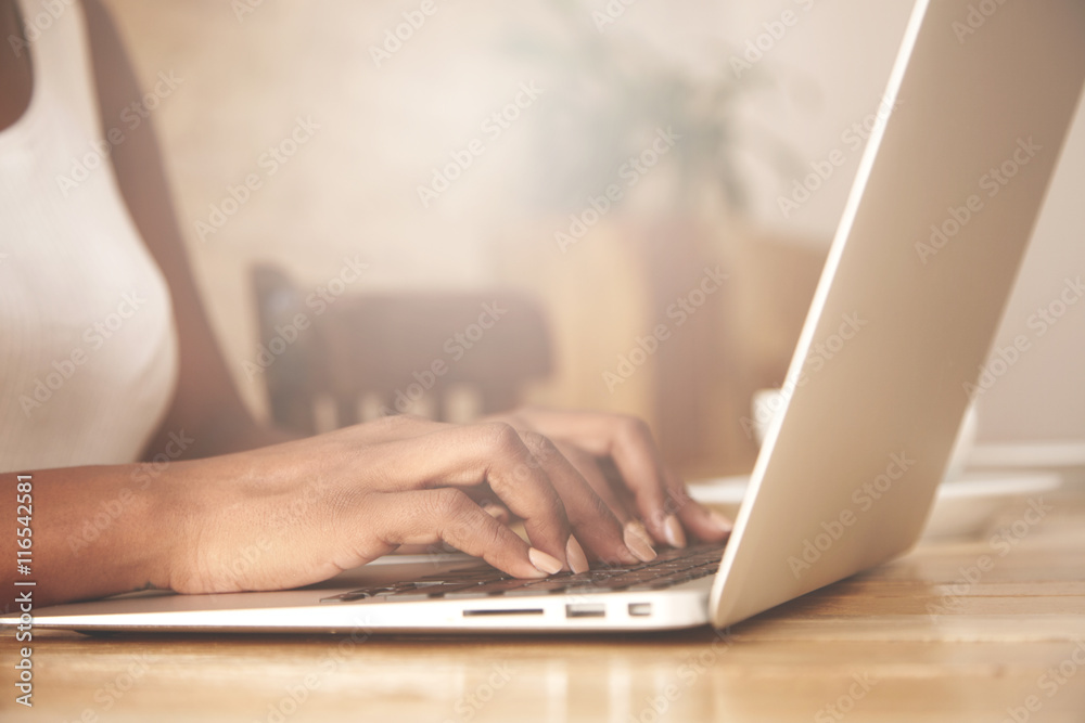 Cropped portrait of African female blogger keyboarding on laptop computer, posting a new article on her blog. Busy woman hand typing on keyboard while sitting at her working place in the office Cropped portrait of African female blogger keyboarding on laptop computer, posting a new article on her blog. Busy woman hand typing on keyboard while sitting at her working place in the office