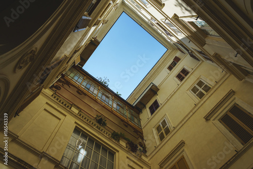 Cozy historic courtyard in the old town of Rome. Windows with shutters vintage, a small balcony and  blue summer sky above. © Evgenii Starkov