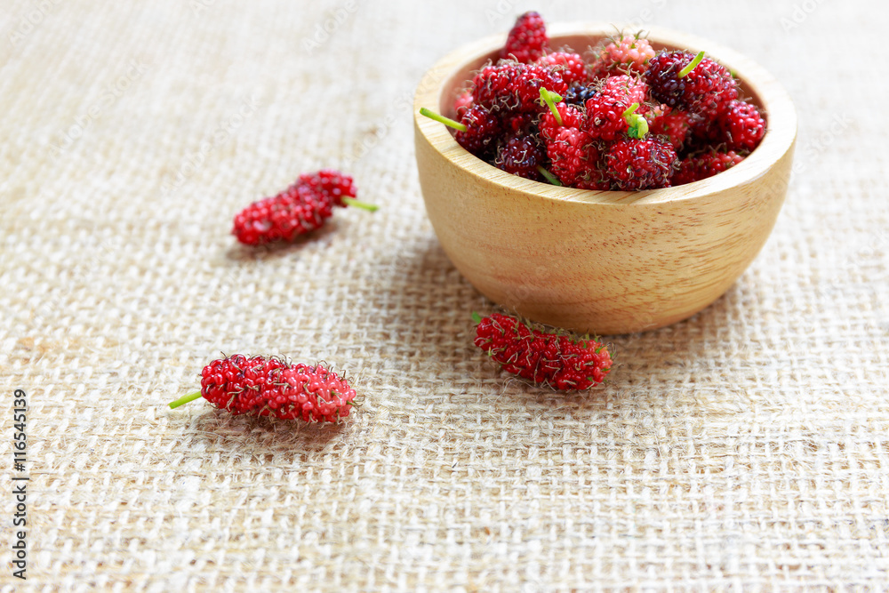 Red mulberry in wooden bowl and on cloth floor Red mulberry in wooden bowl and on cloth floor