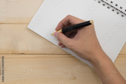 women hand with pen write on blank paper noetbook on wood table background