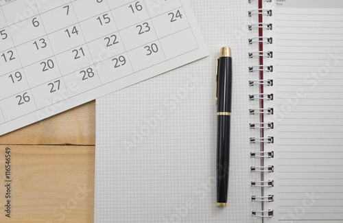 pen, calender and paper natebook on wood table photo