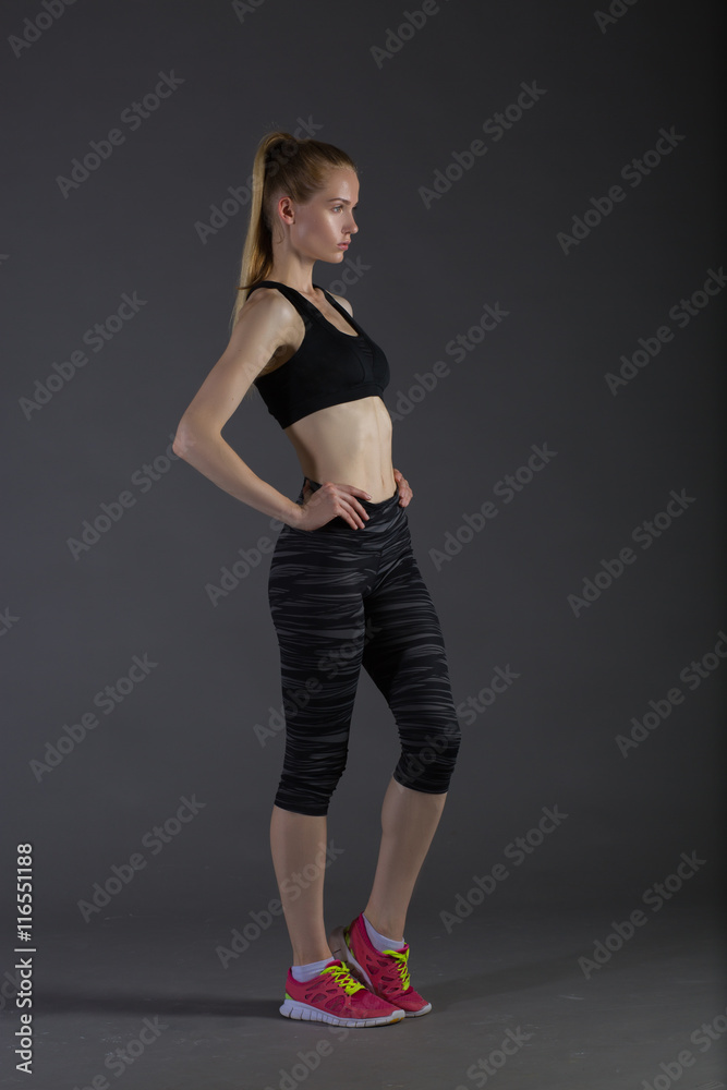 Body of slim female in activewear doing posin on gray low key, perfect blonde Body of slim female in activewear doing posin on gray low key, perfect blonde