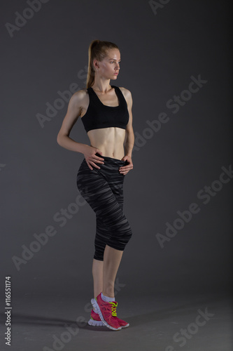 Body of slim female in activewear doing posin on gray low key, perfect blonde