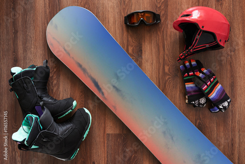 set of snowboard boots, helmet, gloves and mask on wooden