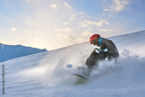 Girl snowboarder slows down the slope on background of sunset