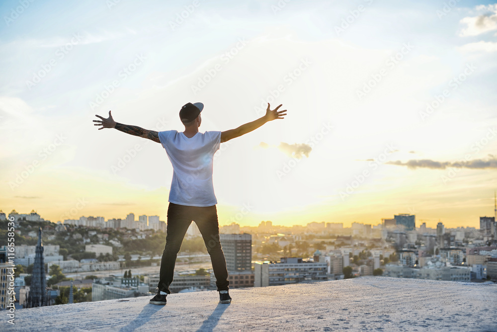 Obraz premium man with open arms facing a city's silhouette at the sunset