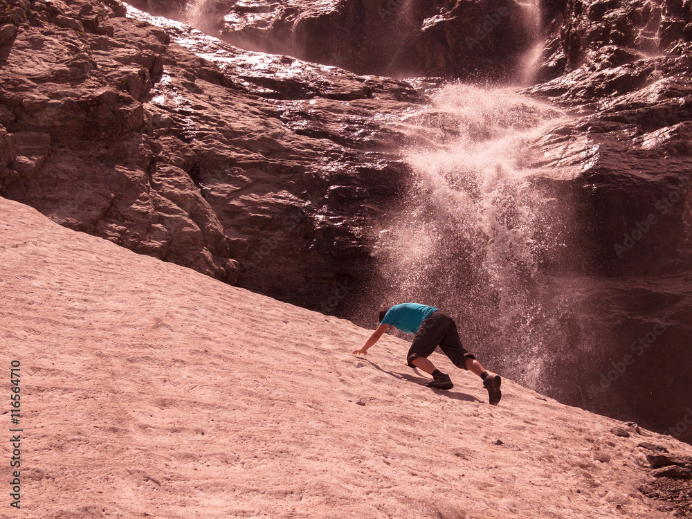 Obraz premium Toned image of an adult male to climb the mountain through the snow against the backdrop of a large waterfall