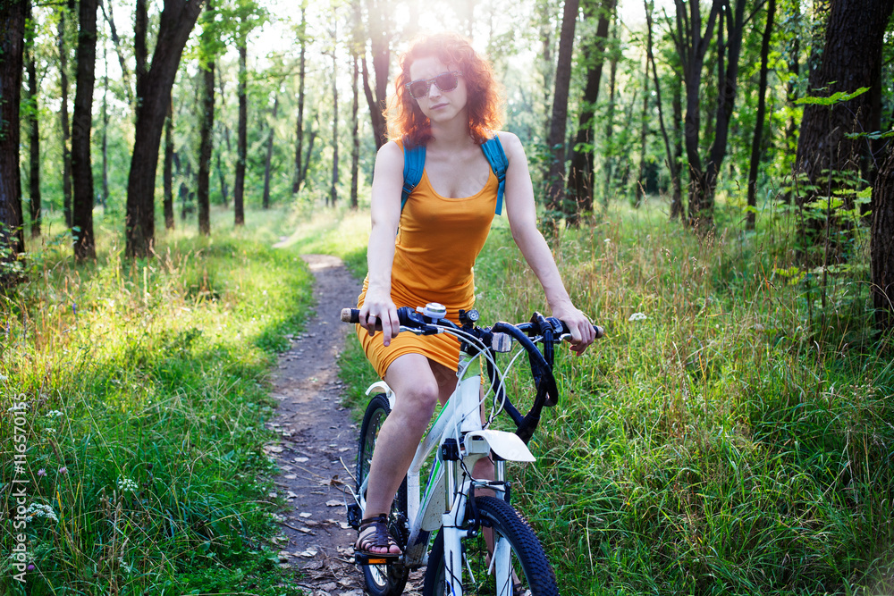 Young redhead woman in sunglasses riding a bike in the city park Young redhead woman in sunglasses riding a bike in the city park