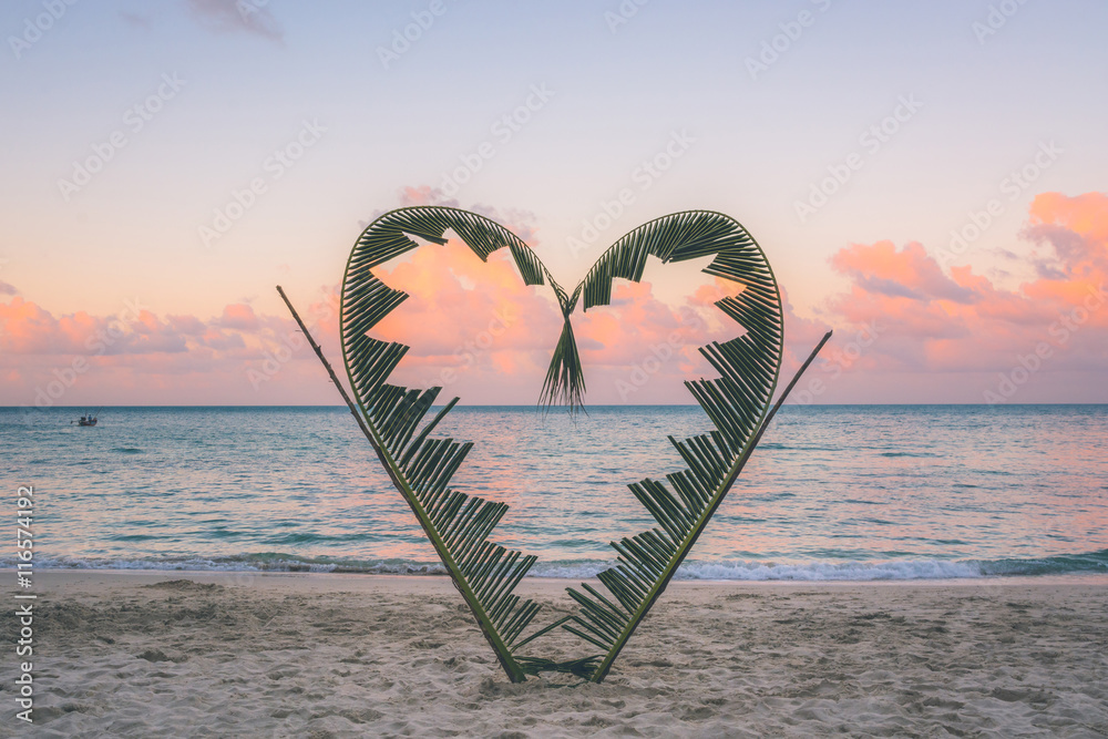 Naklejka premium Palm branches tied into the shape of a heart on the beach.