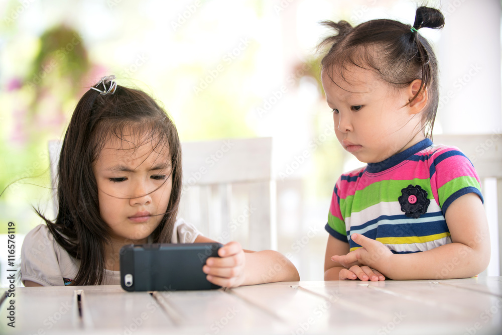 Two serious asian girl sitting on chair looking cell phone Two serious asian girl sitting on chair looking cell phone