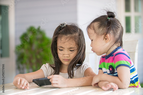 Two little asian girl sitting on chair using cell phone