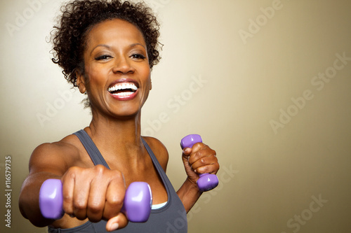 Happy African American fitness woman lifting dumbbells smiling and energetic. photo