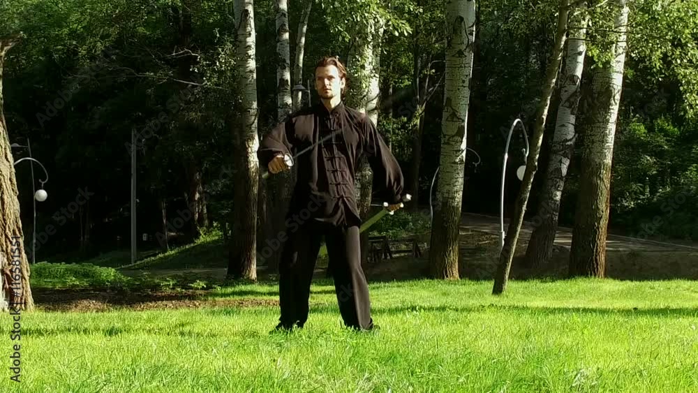 Training in the park. Man practicing elements of tai chi. The young man rotating steel swords around his body. Slow motion. HD Training in the park. Man practicing elements of tai chi. The young man rotating steel swords around his body. Slow motion. HD