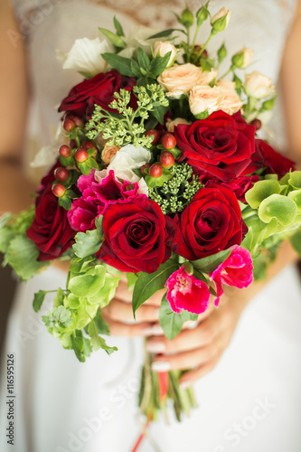 Fototapeta Naklejka Na Ścianę i Meble -  Close up of wedding bouquet of bridal flowers in hands of anonymous bride. Focus on fresh red flowers.