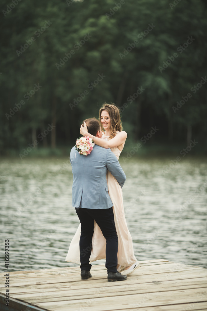 Fototapeta premium Groom carrying bride near lake and forest
