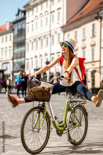 Young female tourist with backpack and hat having fun riding a bicycle in the old city center of Ljubljana in Slovenia