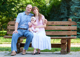 happy family portrait with baby girl on outdoor, sit on wooden bench in city park, summer season, child and parent