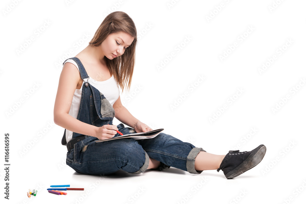 Young woman happily sitting  on the floor drawing in her note pad