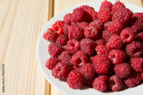 Close up of fresh raspberry on a white plate on wooden boards