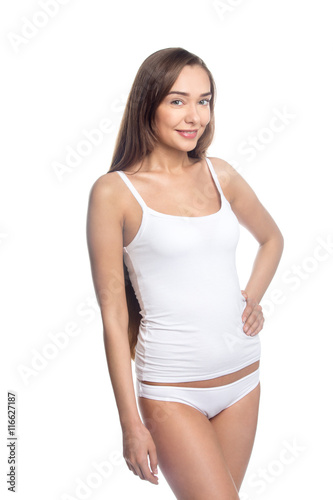 Portrait of beautiful attractive Caucasian young woman wearing white set of undergarments. Smiling girl in tank top and panties standing against white background and looking at camera. Studio shot © fizkes