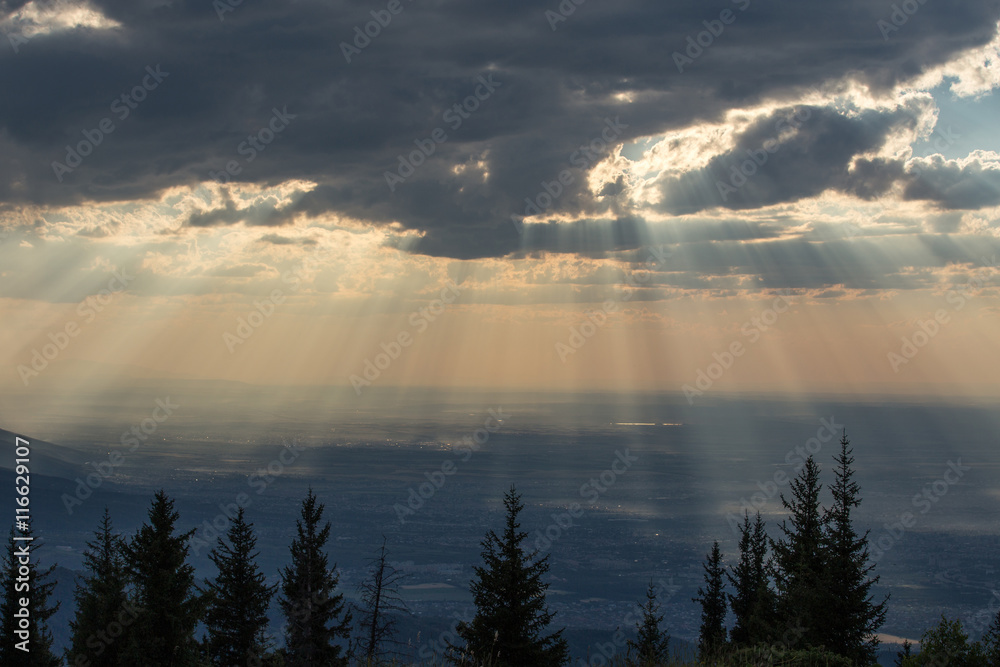 Sunrays through clouds over mountain and city Sunrays through clouds over mountain and city