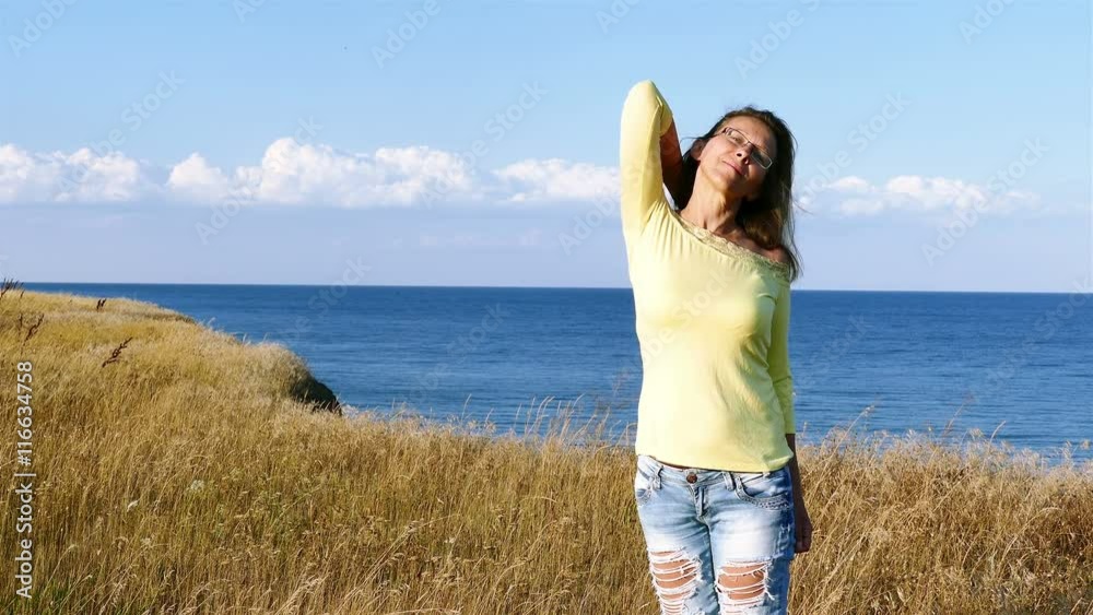 4K. Adult slender woman in yellow blouse corrects hair on seashore. 4K. Adult slender woman in yellow blouse corrects hair on seashore.
