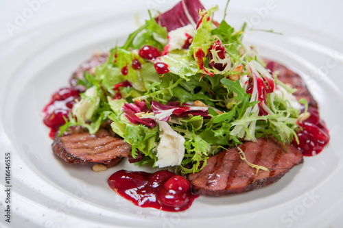 Salad with veal grilled, fresh lettuce and arugula, sweet and sour cherry sauce on white round plate