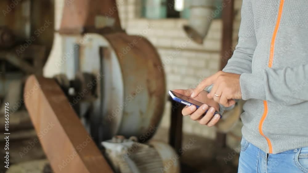 Male hand is holding a modern touch screen phone and blur image of old factory Male hand is holding a modern touch screen phone and blur image of old factory