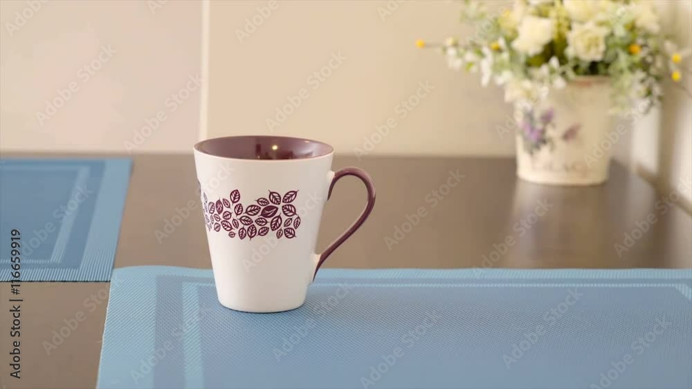 A white coffee cup on top of the table with the leaves as a design on it A white coffee cup on top of the table with the leaves as a design on it