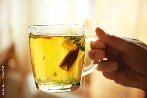 Female hand holding cup with green tea on blurred kitchen background