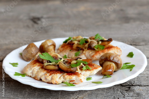 Roasted Turkey fillet with cheese and mushrooms on a plate and on old wooden background. Delicious Turkey cutlets recipe. Closeup