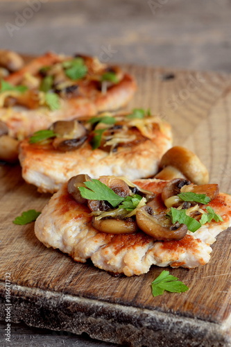 Slices of roasted Turkey meat. Fried Turkey steaks with cheese and mushrooms on a chopping board and an old wooden table. Delicious and easy meat recipe. Closeup