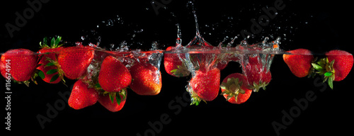 Strawberries splashing into water on a black background © olex_1980