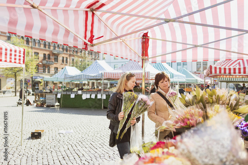 Mature women buying flowers at market stall in town square photo