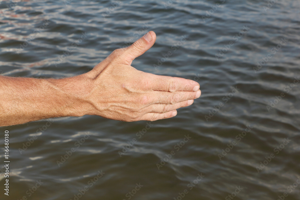 Suntanned male hand against a surface of the water
