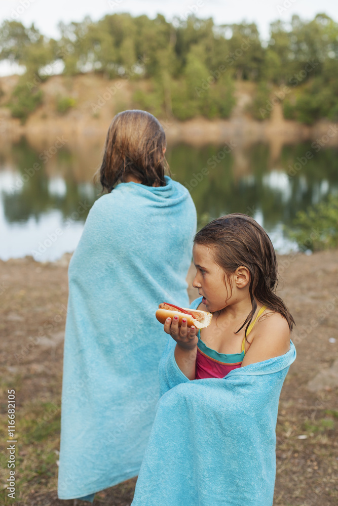 Two girls wrapped in blue towels standing by lake Two girls wrapped in blue towels standing by lake