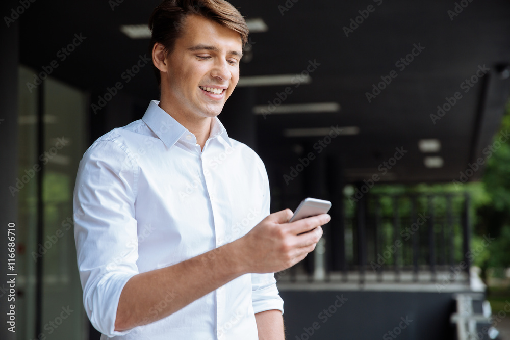 Happy businessman using smartphone and smiling near business center Happy businessman using smartphone and smiling near business center