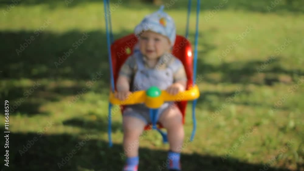 Adorable baby boy with big beautiful eyes having fun on a swing ride at a playground in a sunny summer park Adorable baby boy with big beautiful eyes having fun on a swing ride at a playground in a sunny summer park