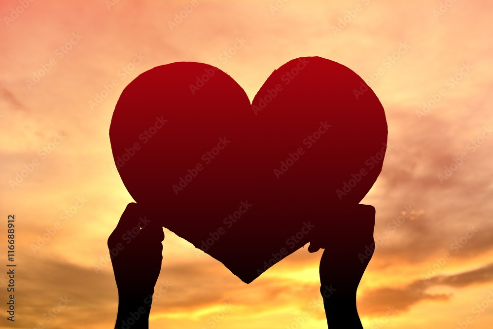 Silhouette boy holding heart shape at sunset