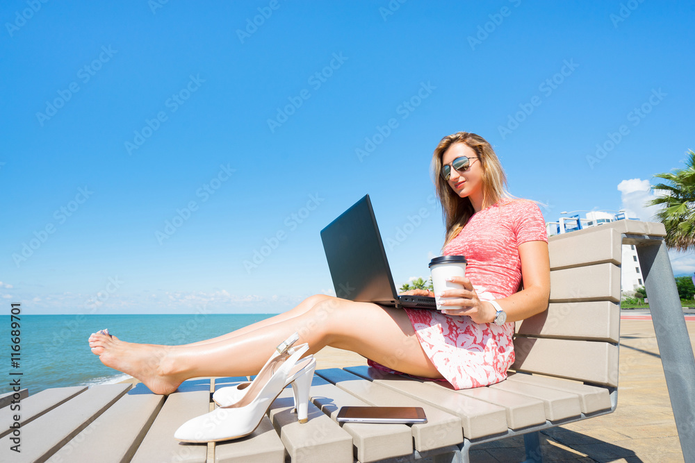 Young beautiful woman sitting on the beach chiar  with laptop , smartphone and shoes, and drink coffee.