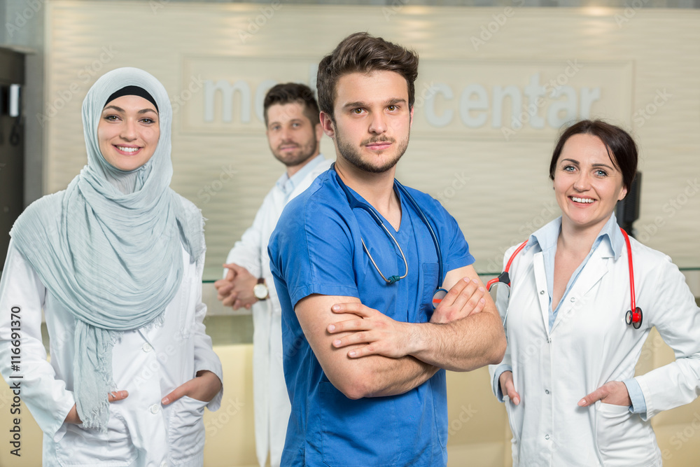 healthcare and medicine concept - attractive male doctor in front of medical group in hospital showing thumbs up healthcare and medicine concept - attractive male doctor in front of medical group in hospital showing thumbs up