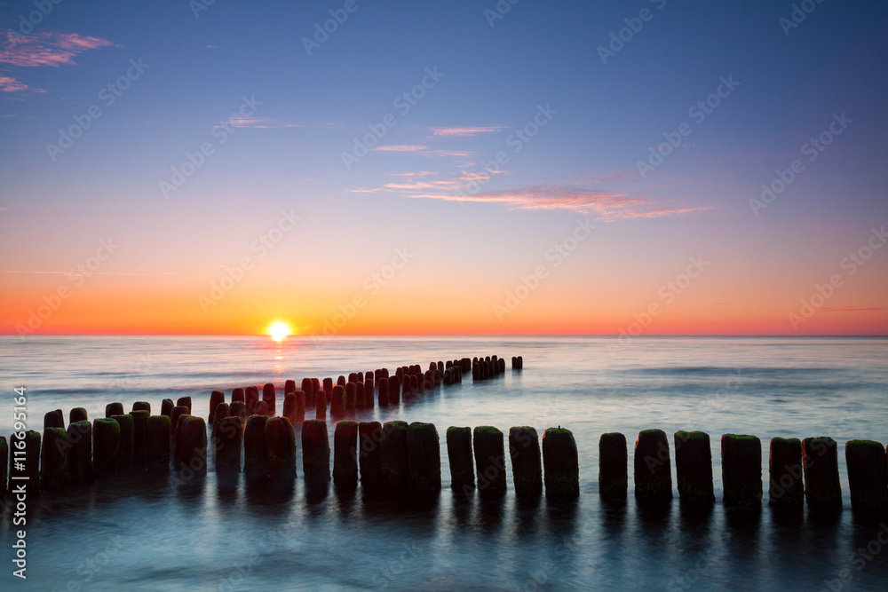 Sunset at Baltic sea, view on old breakwater piles.