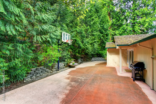 House exterior. Concrete back yard with patio area and basketball hoop.