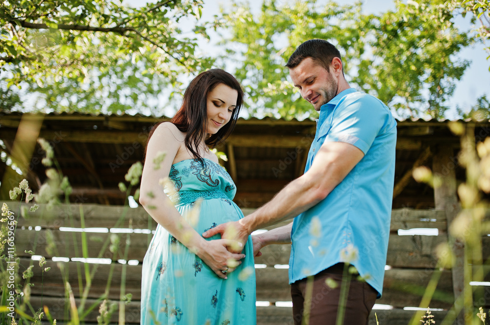 Fototapeta premium Happy pregnant couple at turquoise dress on the garden