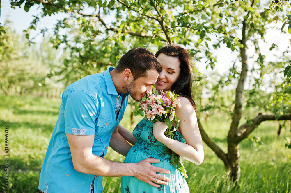 Happy pregnant couple at turquoise dress on the garden Happy pregnant couple at turquoise dress on the garden