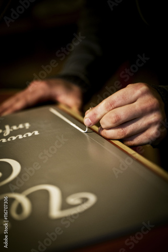 A signwriter working with a loaded brush painting a line freehand on the edge of a sign. 